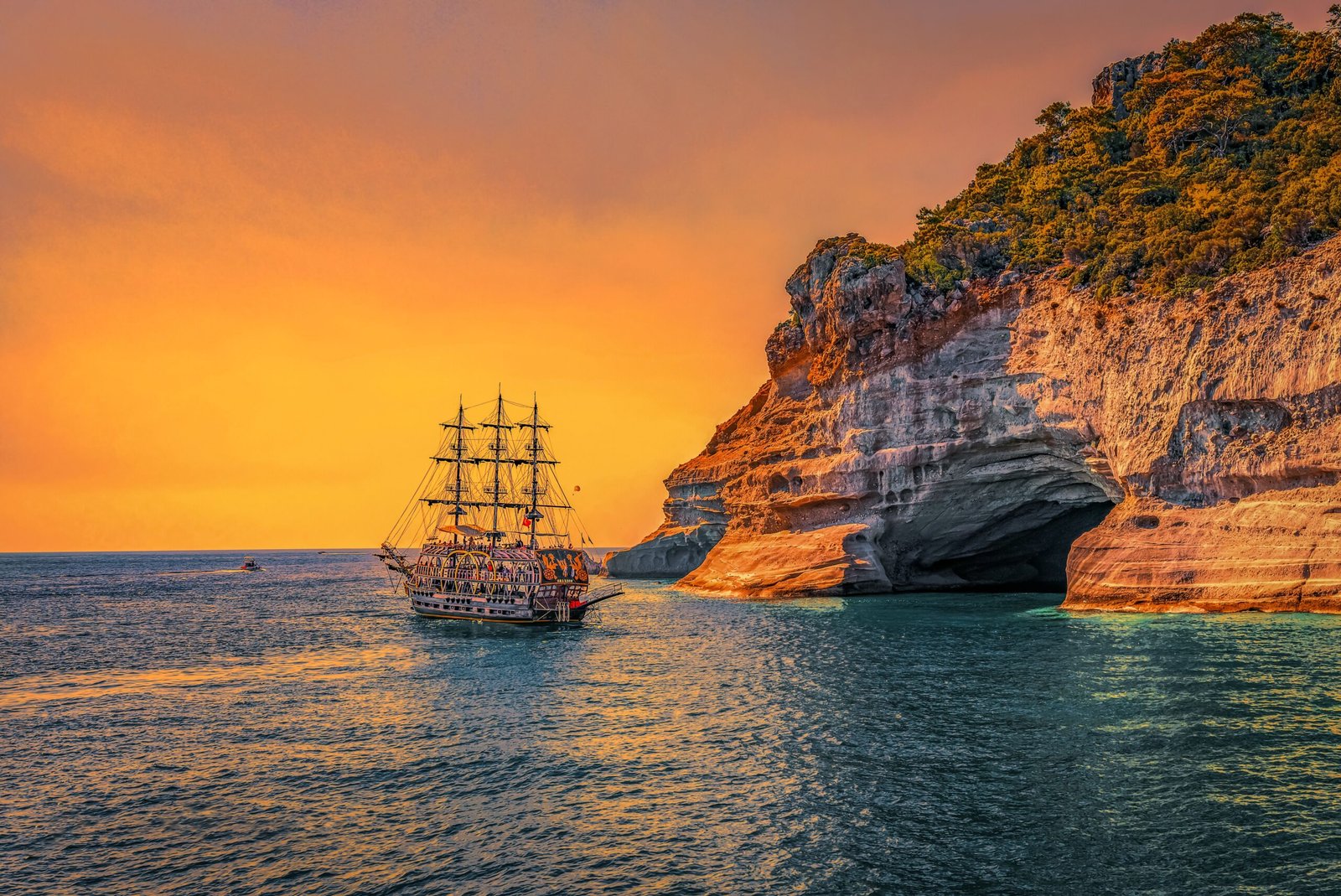 A majestic sailing ship navigates past stunning sea cliffs at sunset, offering a picturesque view of adventure.